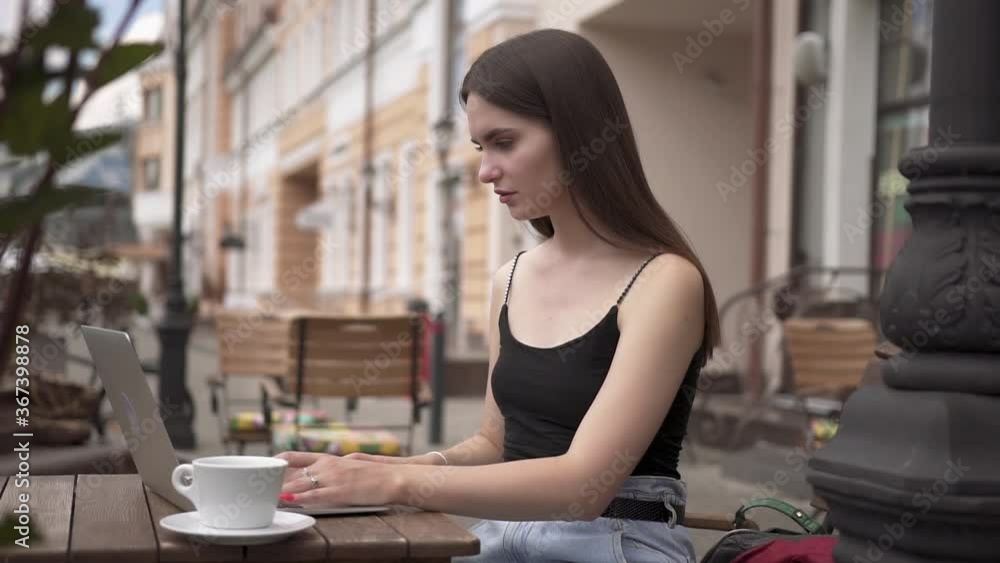 Attractive student girl using laptop in outdoors cafe. Young girl freelance is working with laptop in cafe. Modern technology and youth concept. Attractive student girl using laptop in outdoors cafe. Young girl freelance is working with laptop in cafe. Modern technology and youth concept.