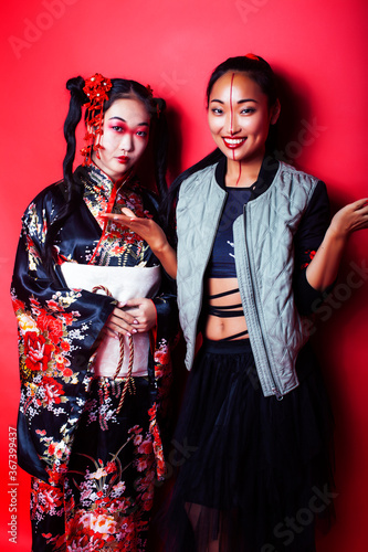 two pretty geisha girls friends: modern asian woman and traditional wearing kimono posing cheerful on red background