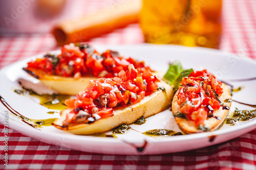 Traditional Italian bruschetta with cherry tomatoes, pesto sauce and balsamic vinegar on white plate. Close up