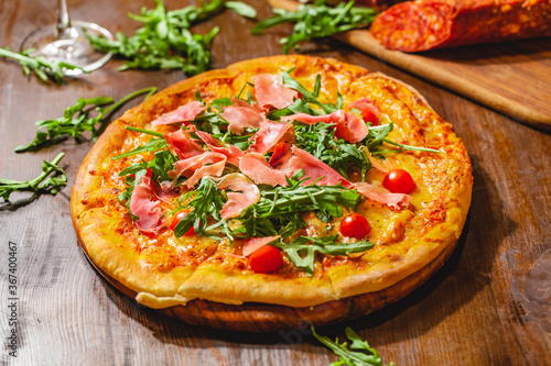 Italian pizza with prosciutto (parma ham), arugula (salad rocket) and cherry tomatoes on wooden board. Close up