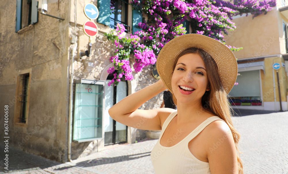 Close up of young tourist woman holding hat visiting Sirmione old flowered town on Lake Garda, Italy