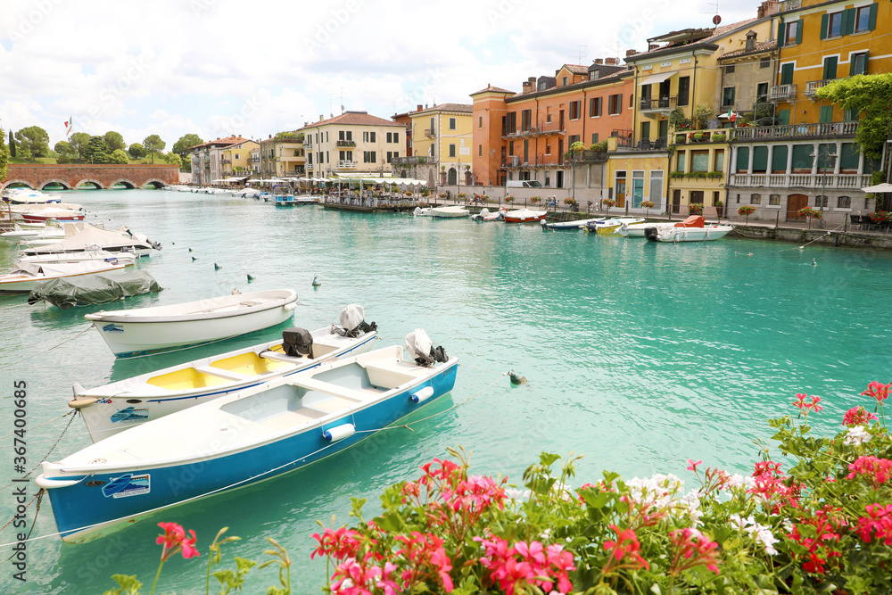 PESCHIERA DEL GARDA, ITALY - JUNE 19, 2020: Peschiera del Garda colorful and flowered harbor with boats moored Lake Garda, Italy