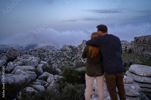 Rear view of couple looking at rocky mountain while standing against cloudy sky