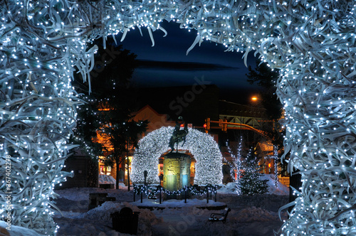 Brightly lit Elk antler arches in Jackson Wyoming town square in winter at twilight with cowboy on bucking broncho statue photo
