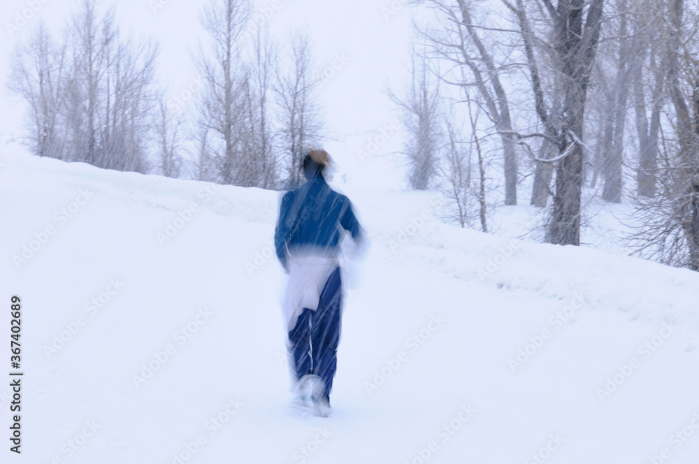 Young female jogger running in a snowstorm on Gross Ventre Road Wyoming with Cottonwood forest