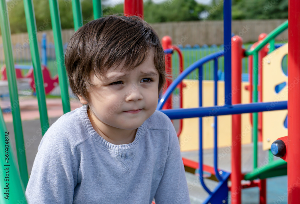 Portrait Cute litte boy sitting alone in playground, Candid Child boy looking out deep in through outdoors play area in sunny day summer Portrait Cute litte boy sitting alone in playground, Candid Child boy looking out deep in through outdoors play area in sunny day summer