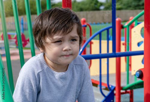 Portrait Cute litte boy sitting alone in playground, Candid Child boy looking out deep in through outdoors play area in sunny day summer