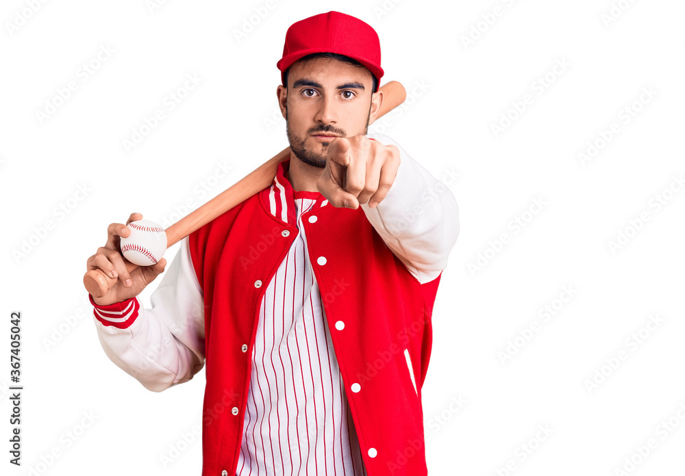 Young handsome man holding baseball bat and ball pointing with finger to the camera and to you, confident gesture looking serious Young handsome man holding baseball bat and ball pointing with finger to the camera and to you, confident gesture looking serious