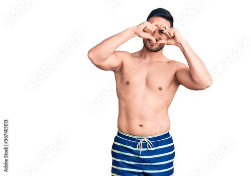 Young handsome man wearing swimwear doing heart shape with hand and fingers smiling looking through sign