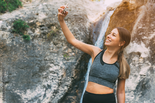 Beautiful slim woman doing sport in the morning in a river, taking a picture on the phone, exploring nature, smiling happily healthy lifestyle