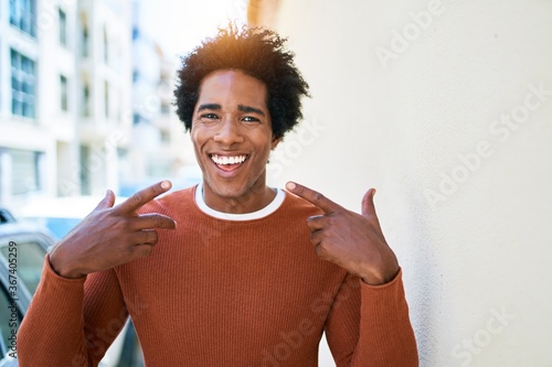 Young handsome african american man wearing casual clothes smiling happy. Standing with big smile on face pointing mouth with fingers walking at town street.