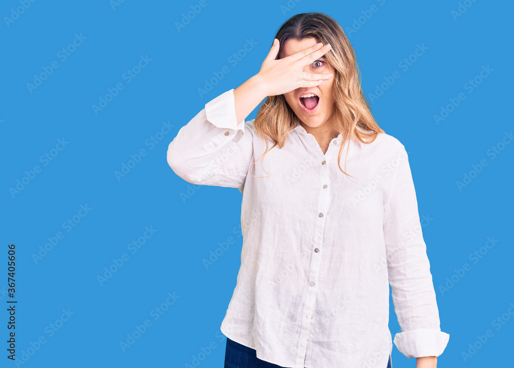 Young caucasian woman wearing casual clothes peeking in shock covering face and eyes with hand, looking through fingers with embarrassed expression. Young caucasian woman wearing casual clothes peeking in shock covering face and eyes with hand, looking through fingers with embarrassed expression.