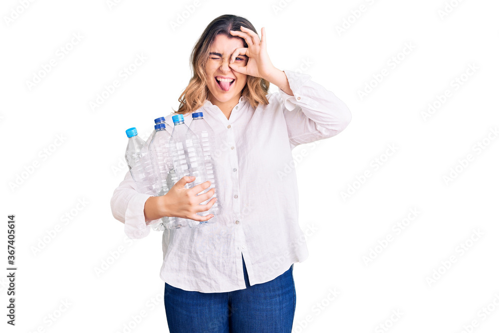 Young caucasian woman holding recycling plastic bottles smiling happy doing ok sign with hand on eye looking through fingers Young caucasian woman holding recycling plastic bottles smiling happy doing ok sign with hand on eye looking through fingers