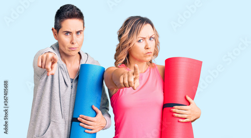 Couple of women holding yoga mat pointing with finger to the camera and to you, confident gesture looking serious © Krakenimages.com