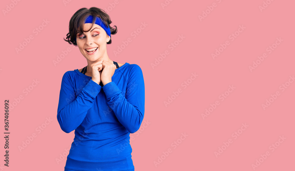 Beautiful young woman with short hair wearing training workout clothes laughing nervous and excited with hands on chin looking to the side Beautiful young woman with short hair wearing training workout clothes laughing nervous and excited with hands on chin looking to the side