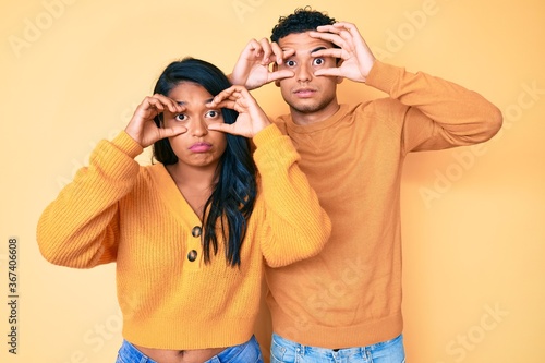 Beautiful latin young couple wearing casual clothes together trying to open eyes with fingers, sleepy and tired for morning fatigue