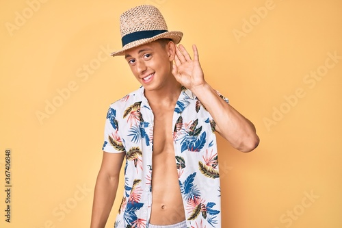 Young hispanic boy wearing summer hat smiling with hand over ear listening and hearing to rumor or gossip. deafness concept.