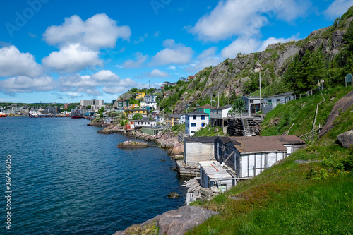 St. John's, NL / Canada - July 2020: Houses along the hillside of St. John's Harbour. The houses are colorful and stacked on top of each other. The water is bright blue. The sky is blue and cloudy. 