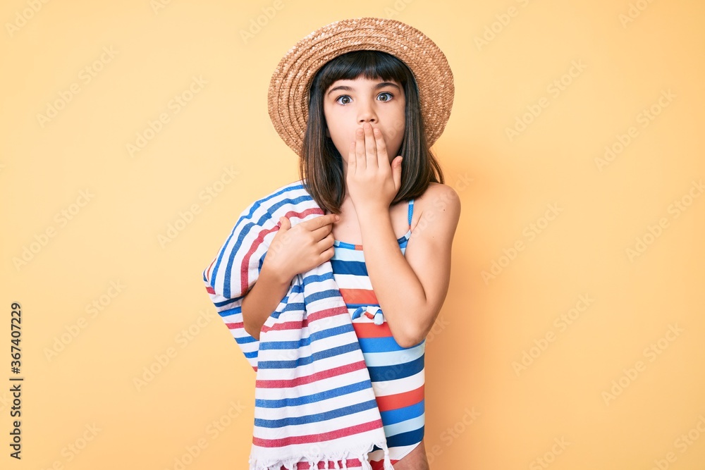 Young little girl with bang wearing swimsuit and summer hat holding towel covering mouth with hand, shocked and afraid for mistake. surprised expression Young little girl with bang wearing swimsuit and summer hat holding towel covering mouth with hand, shocked and afraid for mistake. surprised expression