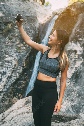 Beautiful slim woman doing sport in the morning in a river  taking a picture on the phone  exploring nature  smiling happily healthy lifestyle