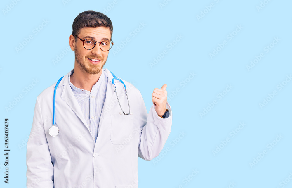 Handsome young man with bear wearing doctor uniform smiling with happy face looking and pointing to the side with thumb up. Handsome young man with bear wearing doctor uniform smiling with happy face looking and pointing to the side with thumb up.