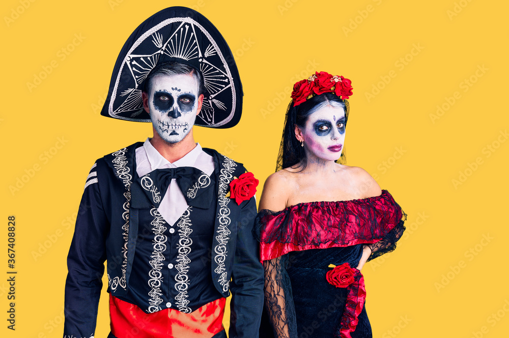 Young couple wearing mexican day of the dead costume over background relaxed with serious expression on face. simple and natural looking at the camera.