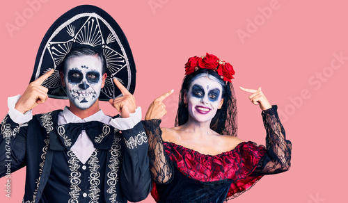Young couple wearing mexican day of the dead costume over background smiling pointing to head with both hands finger, great idea or thought, good memory