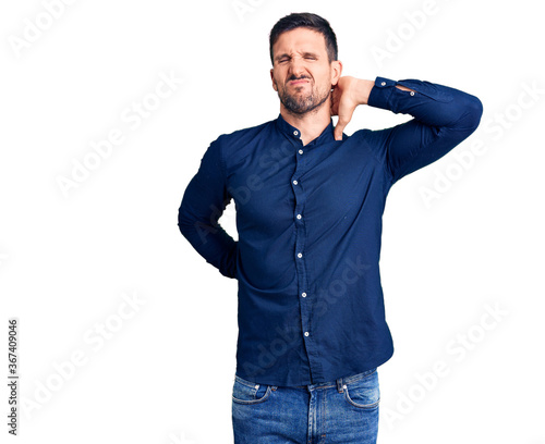 Young handsome man wearing casual shirt suffering of neck ache injury, touching neck with hand, muscular pain