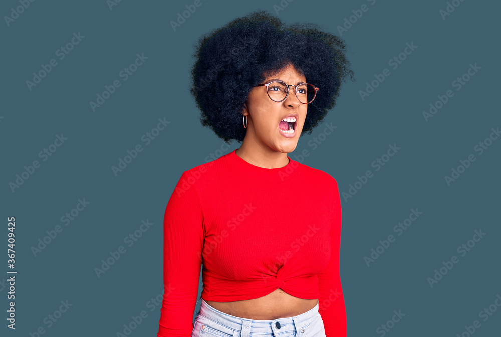 Young african american girl wearing casual clothes and glasses angry and mad screaming frustrated and furious, shouting with anger. rage and aggressive concept. Young african american girl wearing casual clothes and glasses angry and mad screaming frustrated and furious, shouting with anger. rage and aggressive concept.