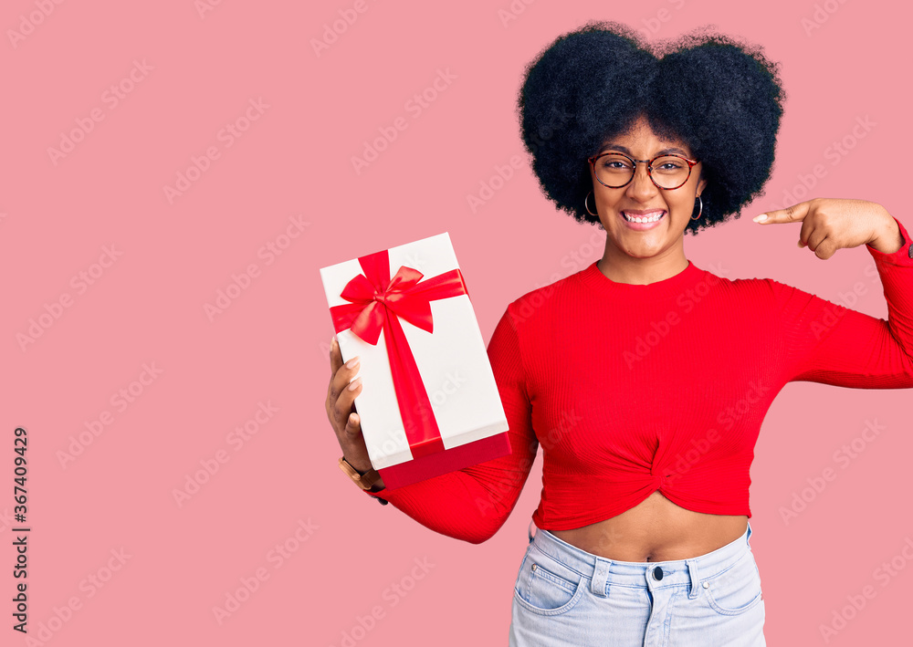 Young african american girl holding gift smiling cheerful showing and pointing with fingers teeth and mouth. dental health concept. Young african american girl holding gift smiling cheerful showing and pointing with fingers teeth and mouth. dental health concept.