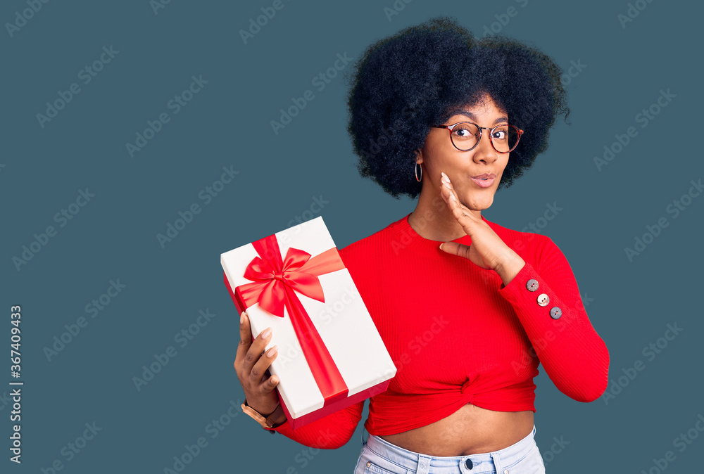 Young african american girl holding gift hand on mouth telling secret rumor, whispering malicious talk conversation Young african american girl holding gift hand on mouth telling secret rumor, whispering malicious talk conversation