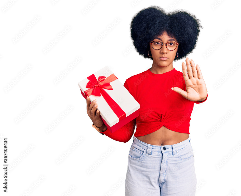 Young african american girl holding gift doing stop sing with palm of the hand. warning expression with negative and serious gesture on the face. Young african american girl holding gift doing stop sing with palm of the hand. warning expression with negative and serious gesture on the face.