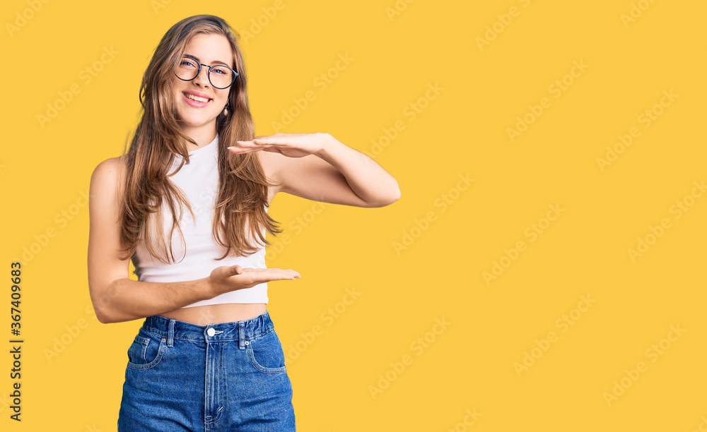 Beautiful caucasian young woman wearing casual clothes and glasses gesturing with hands showing big and large size sign, measure symbol. smiling looking at the camera. measuring concept. Beautiful caucasian young woman wearing casual clothes and glasses gesturing with hands showing big and large size sign, measure symbol. smiling looking at the camera. measuring concept.
