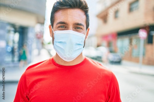 Young handsome hispanic man wearing covid-19 protection medical mask standing at town street.