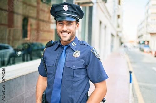 Fotografiet Young handsome hispanic policeman wearing police uniform smiling happy Standing with smile on face at town street