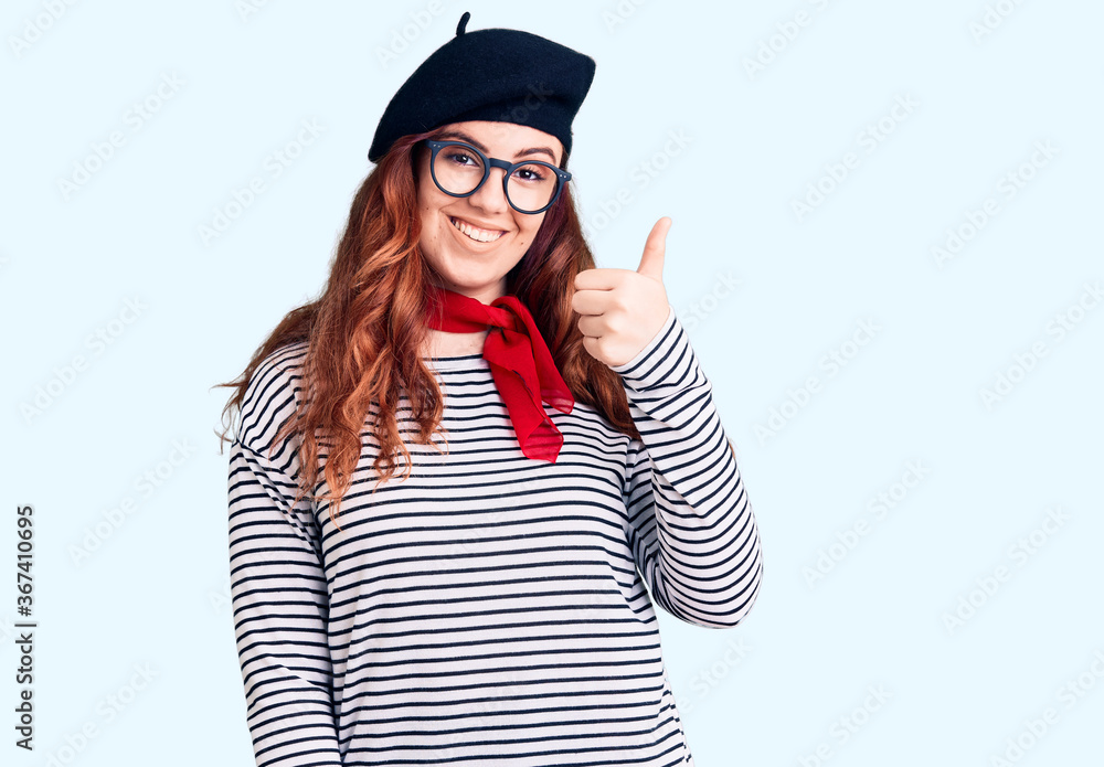 Young beautiful woman wearing french look with beret smiling happy and positive, thumb up doing excellent and approval sign Young beautiful woman wearing french look with beret smiling happy and positive, thumb up doing excellent and approval sign