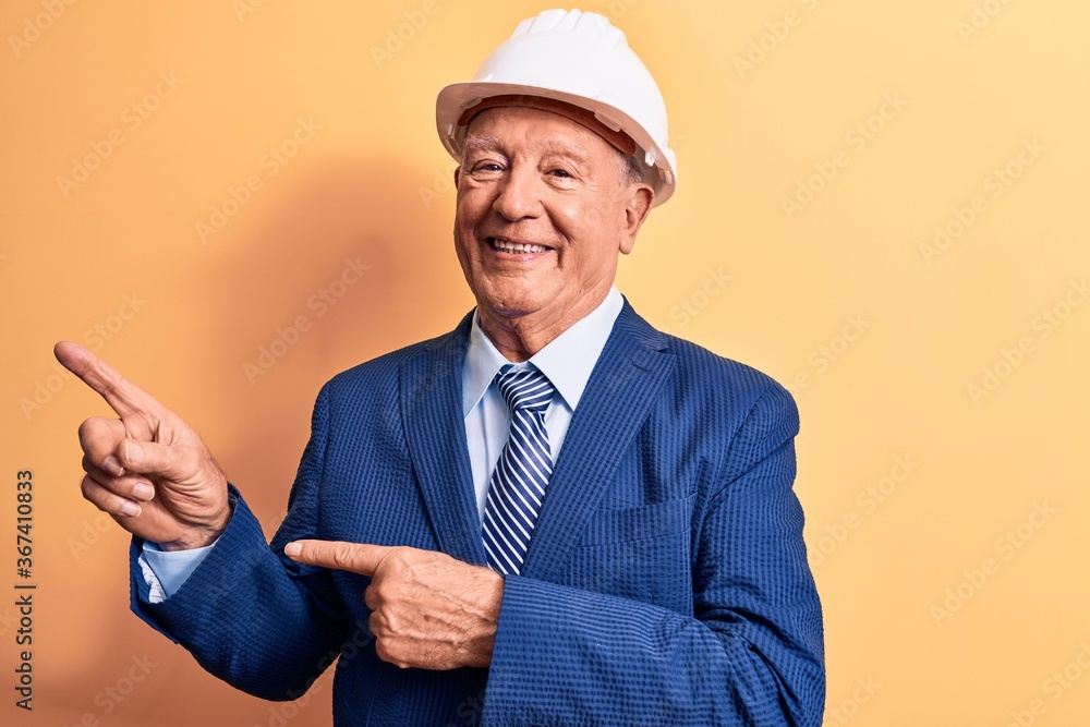 Senior grey-haired architect man wearing suit and security hardhat over yellow background smiling and looking at the camera pointing with two hands and fingers to the side. Senior grey-haired architect man wearing suit and security hardhat over yellow background smiling and looking at the camera pointing with two hands and fingers to the side.