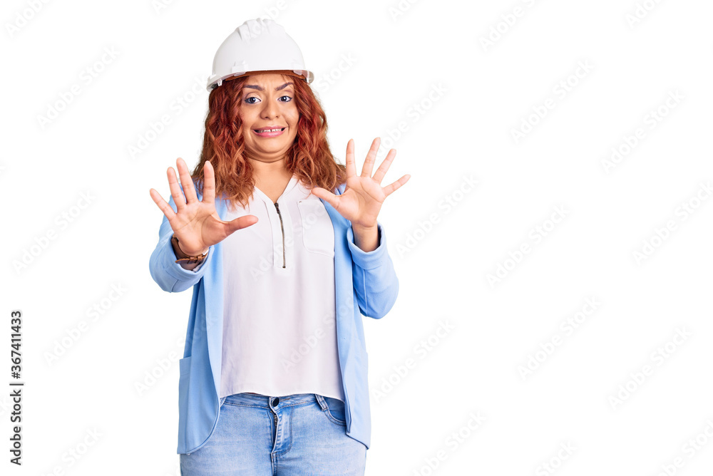 Young latin woman wearing architect hardhat afraid and terrified with fear expression stop gesture with hands, shouting in shock. panic concept. Young latin woman wearing architect hardhat afraid and terrified with fear expression stop gesture with hands, shouting in shock. panic concept.