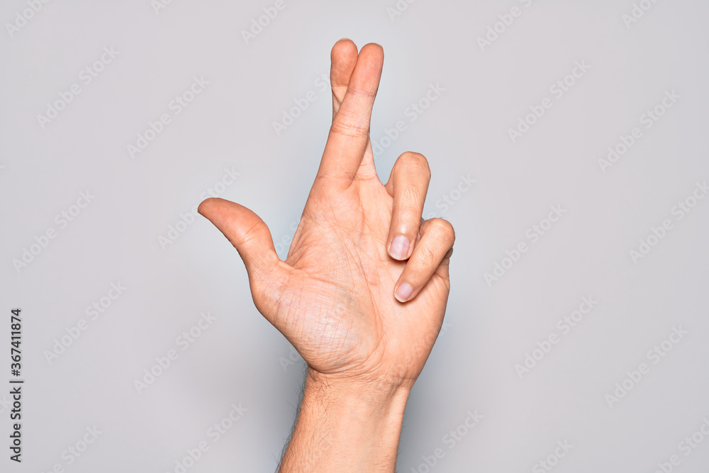 Hand of caucasian young man showing fingers over isolated white background gesturing fingers crossed, superstition and lucky gesture, lucky and hope expression Hand of caucasian young man showing fingers over isolated white background gesturing fingers crossed, superstition and lucky gesture, lucky and hope expression
