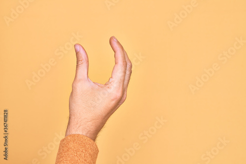 Hand of caucasian young man showing fingers over isolated yellow background picking and taking invisible thing, holding object with fingers showing space