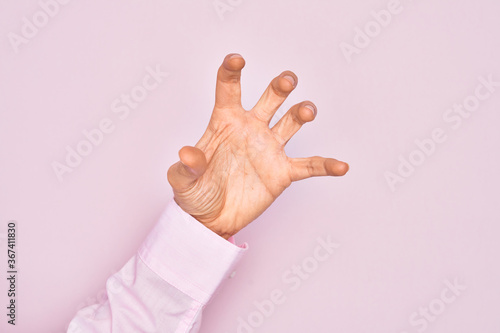 Hand of caucasian young man showing fingers over isolated pink background grasping aggressive and scary with fingers, violence and frustration