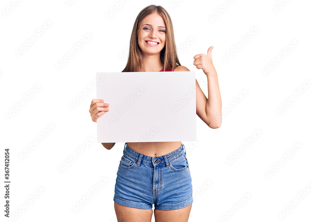 Young beautiful blonde woman holding blank empty banner smiling happy and positive, thumb up doing excellent and approval sign Young beautiful blonde woman holding blank empty banner smiling happy and positive, thumb up doing excellent and approval sign