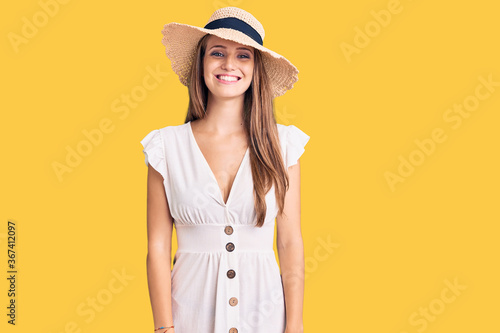 Young beautiful blonde woman wearing summer dress and hat with a happy and cool smile on face. lucky person.