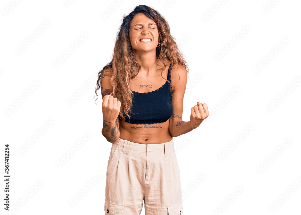 Young hispanic woman with tattoo wearing casual clothes very happy and excited doing winner gesture with arms raised, smiling and screaming for success. celebration concept. Young hispanic woman with tattoo wearing casual clothes very happy and excited doing winner gesture with arms raised, smiling and screaming for success. celebration concept.