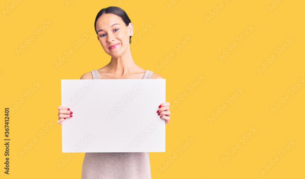 Beautiful brunette young woman holding blank empty banner looking positive and happy standing and smiling with a confident smile showing teeth Beautiful brunette young woman holding blank empty banner looking positive and happy standing and smiling with a confident smile showing teeth