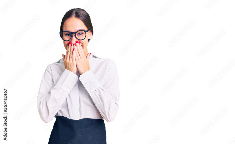 Beautiful brunette young woman wearing professional waitress apron laughing and embarrassed giggle covering mouth with hands, gossip and scandal concept Beautiful brunette young woman wearing professional waitress apron laughing and embarrassed giggle covering mouth with hands, gossip and scandal concept