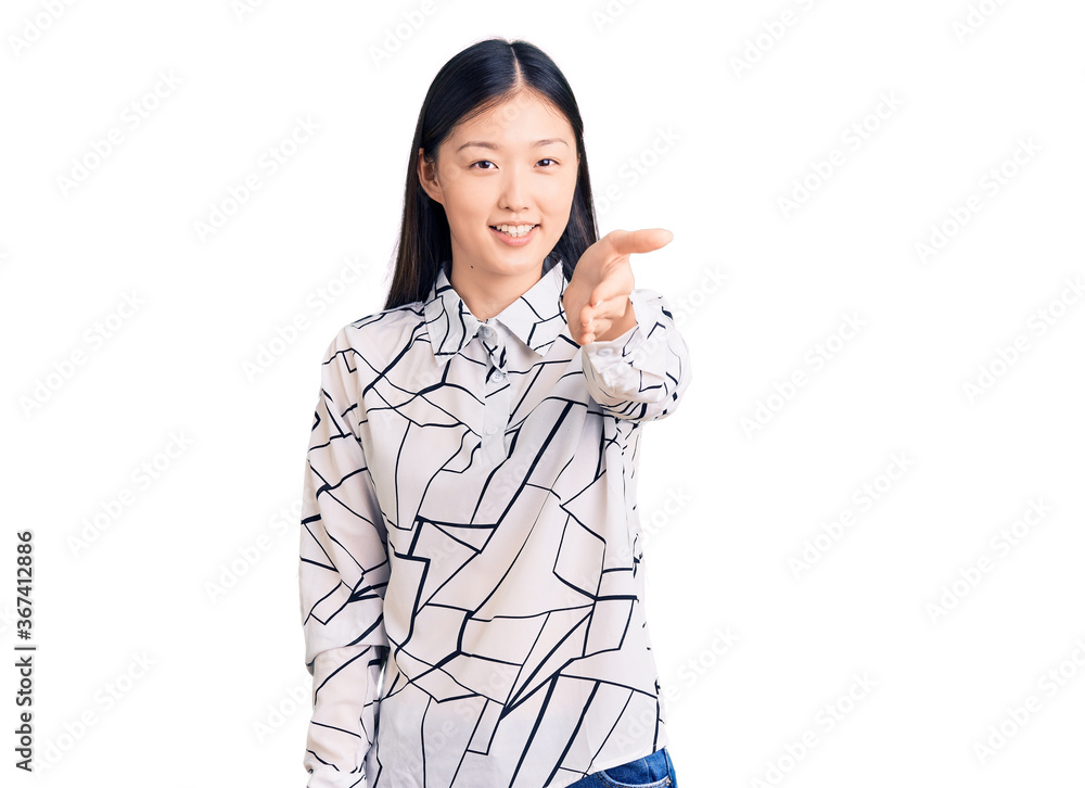Young beautiful chinese woman wearing casual shirt smiling friendly offering handshake as greeting and welcoming. successful business. Young beautiful chinese woman wearing casual shirt smiling friendly offering handshake as greeting and welcoming. successful business.