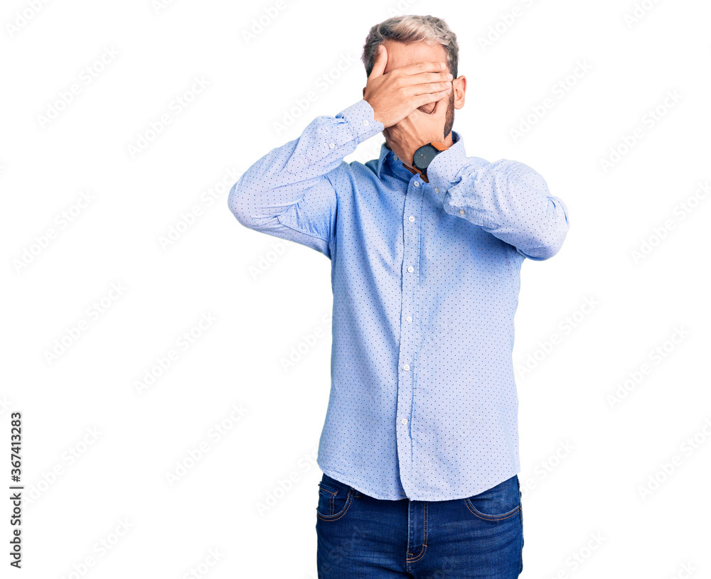 Young handsome blond man wearing elegant shirt covering eyes and mouth with hands, surprised and shocked. hiding emotion Young handsome blond man wearing elegant shirt covering eyes and mouth with hands, surprised and shocked. hiding emotion