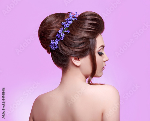 Beauty young woman with flowers in hair. Perfect face skin and makeup. Healthy dark hair decorated with flowers. Beautiful Woman Portrait on pink background. Hair care concept
