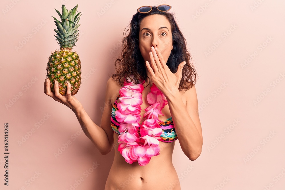 Young beautiful hispanic woman wearing bikini holding pineapple covering mouth with hand, shocked and afraid for mistake. surprised expression Young beautiful hispanic woman wearing bikini holding pineapple covering mouth with hand, shocked and afraid for mistake. surprised expression
